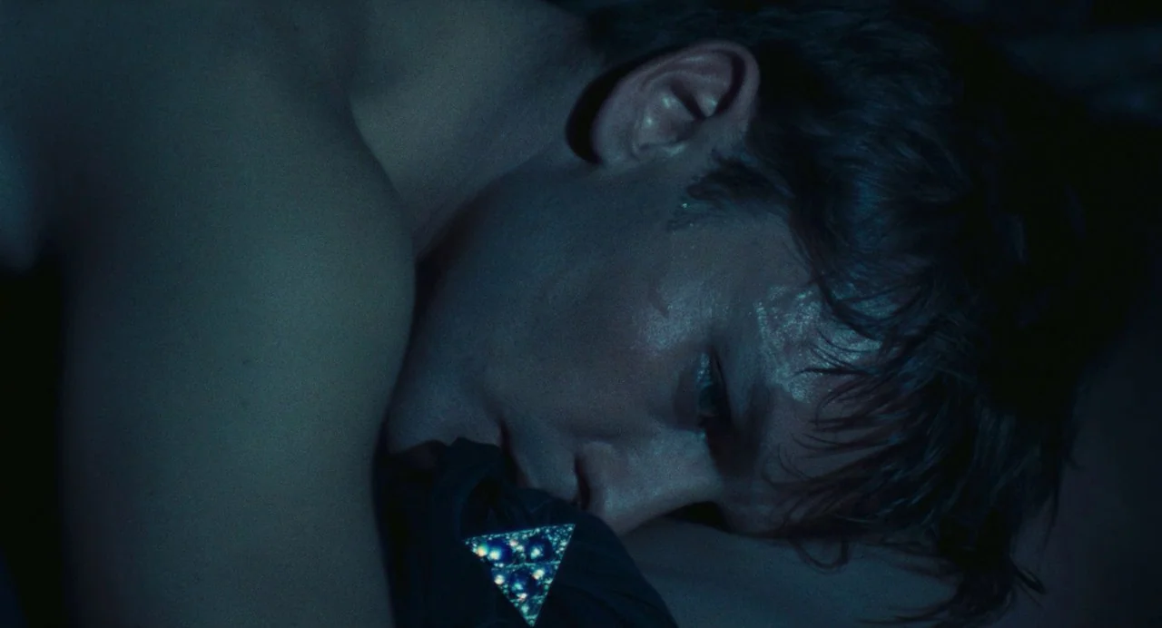 The Damned (1969) movie still: closeup — A dimly lit room with dark blue shadows surrounding a resting person. A man lies horizontally on a bed…