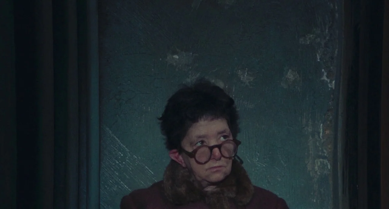 Roma (1972) movie still: medium — A person stands before a rough-textured, dark teal wall in a dim space. The woman looks away from the camera while…