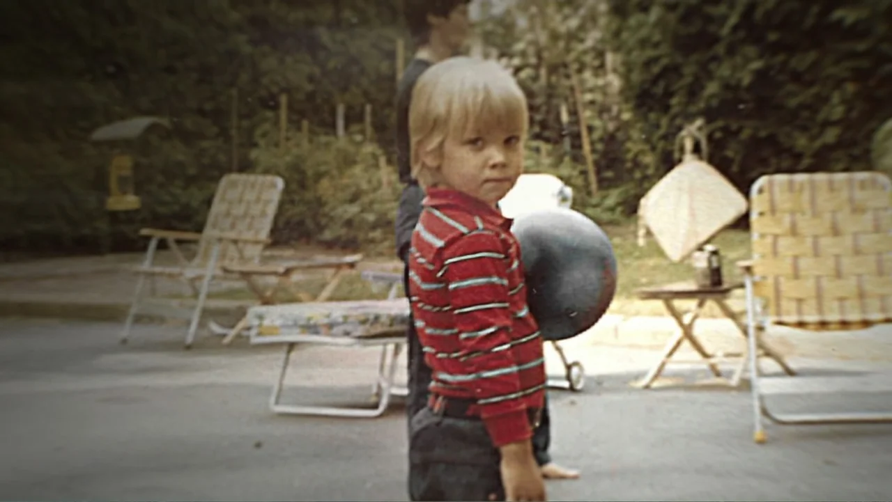 What Happened at Fells Acres? (2023) movie still: medium — A residential backyard features vintage lawn furniture and overgrown foliage in the…
