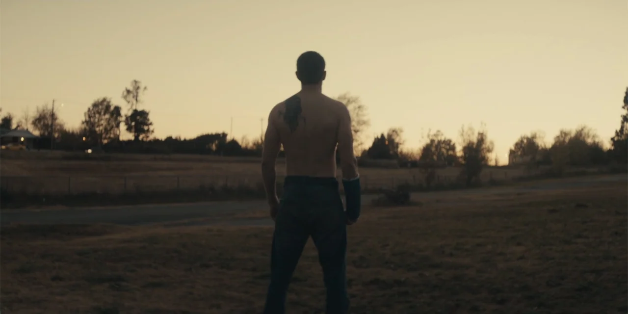 All Roads to Pearla (2019) movie still: fullbody — A man stands alone in a grassy field during the late afternoon. The subject faces away from the…