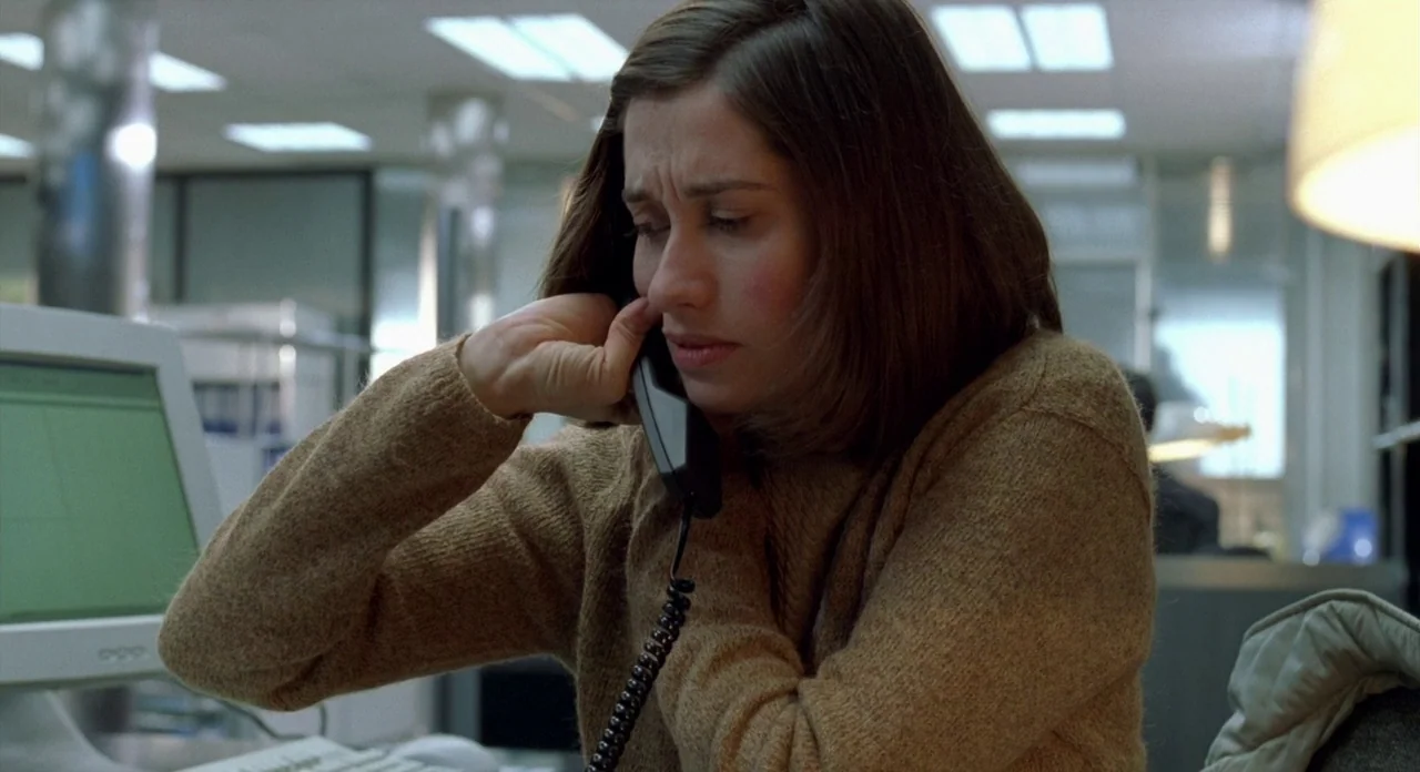 Read My Lips (2001) movie still: medium — An office environment with a computer monitor visible in the left foreground. A young woman in a brown…
