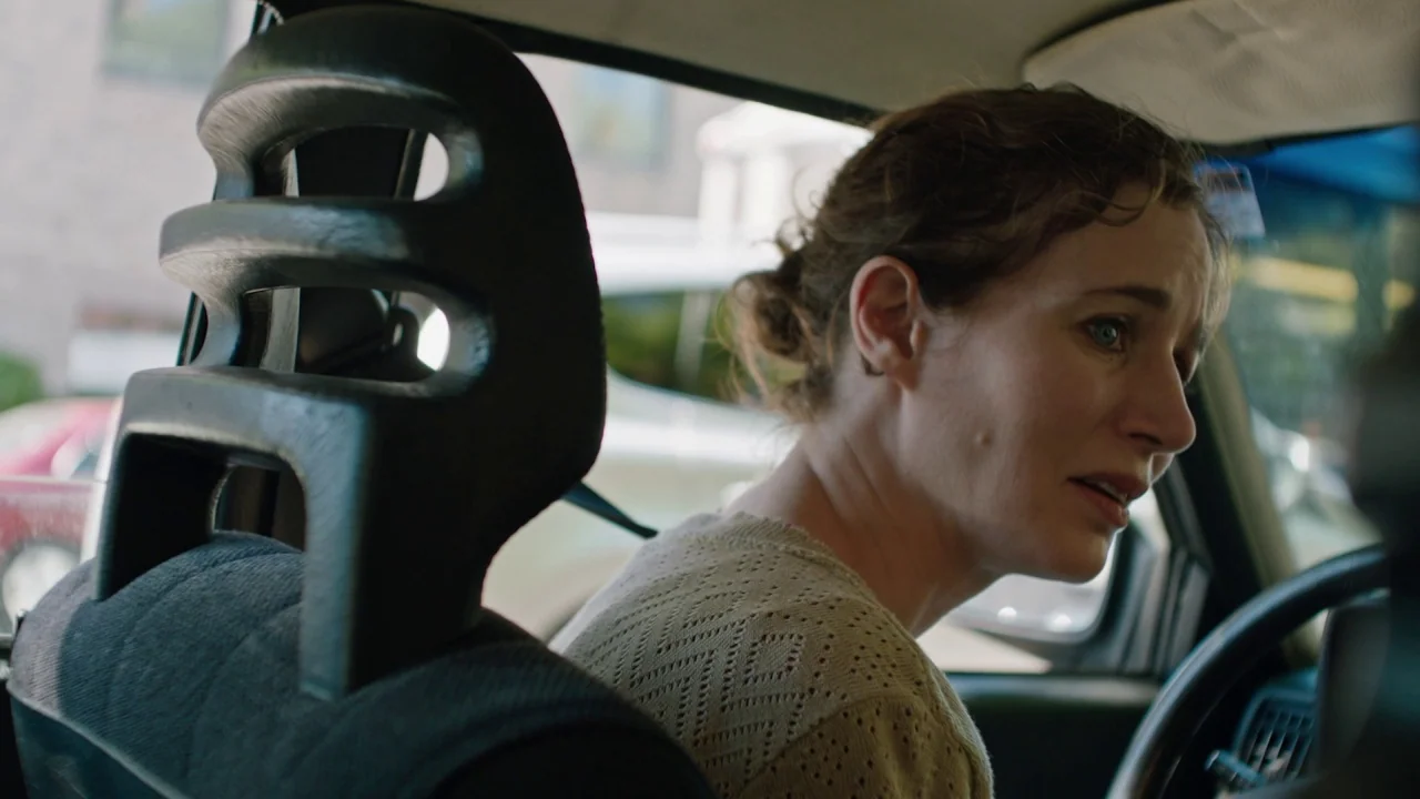 Madeline’s Madeline (2018) movie still: medium — The interior of a car shows a woman sitting in the driver's seat. She turns her head slightly to…