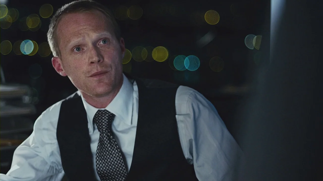 Margin Call (2011) movie still: medium — A dark office at night with large windows showing out-of-focus city lights behind. A man in a dress shirt…