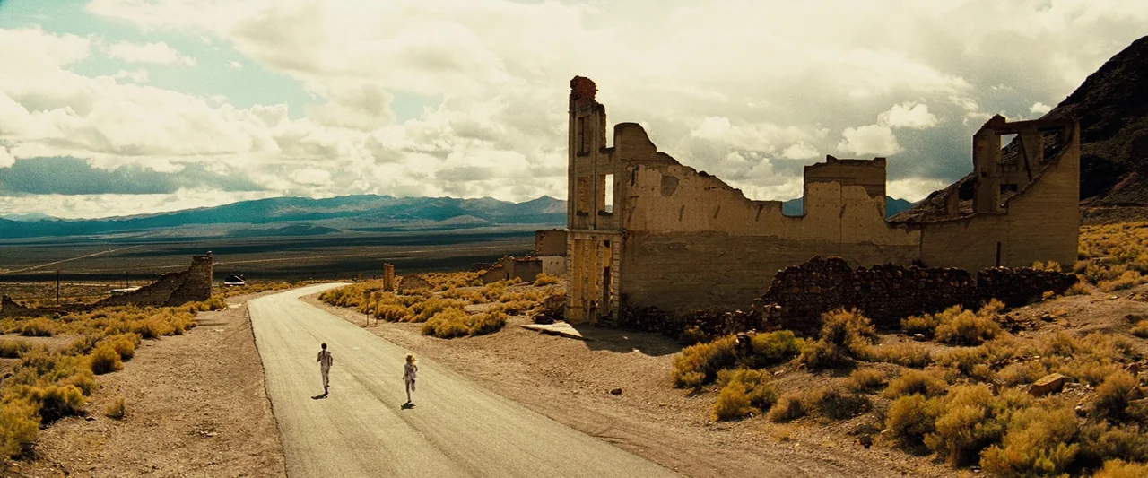 The Island (2005) movie still: wide — A desolate desert landscape features the crumbling stone ruins of a multi-story building. Two figures in white…