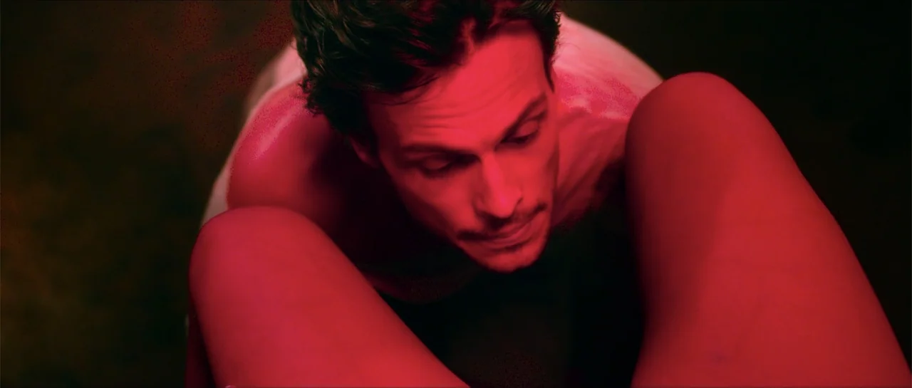 68 Kill (2017) movie still: closeup — An interior space bathed in intense red light focusing on a man. The man leans forward in a high-angle shot…