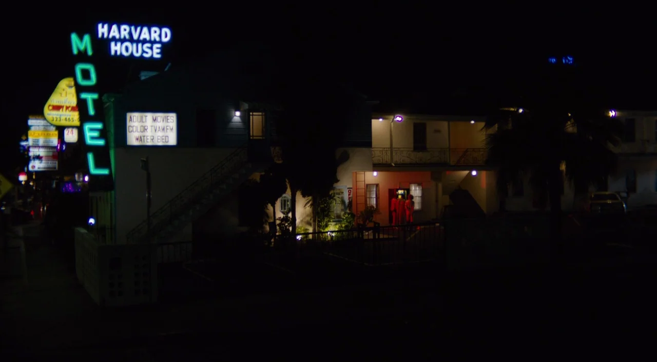 The Greasy Strangler (2016) movie still: wide — A two-story motel building features a prominent glowing neon sign at night. The structure is dark…