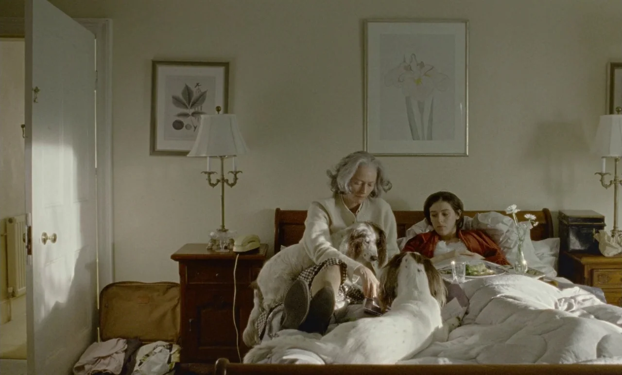 The Souvenir: Part II (2021) movie still: medium — A hotel room with framed botanical art, wood bedside tables, and two beds. An older woman and a…