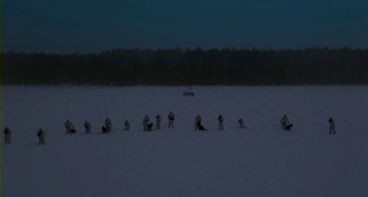 Essential Killing (2010) movie still: wide — A group of soldiers in white camouflage traverses a vast snow-covered field at dawn. A dark line of…