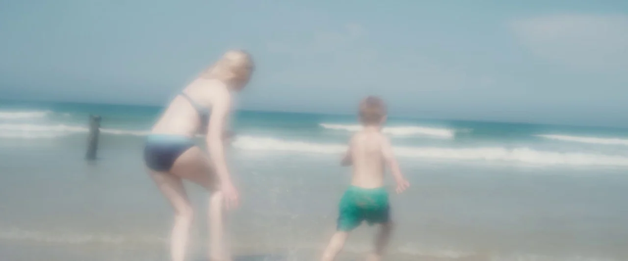 Black Sea (2014) movie still: fullbody — A bright sandy beach with small waves rolling onto the shoreline under clear skies. A teenage girl and a…