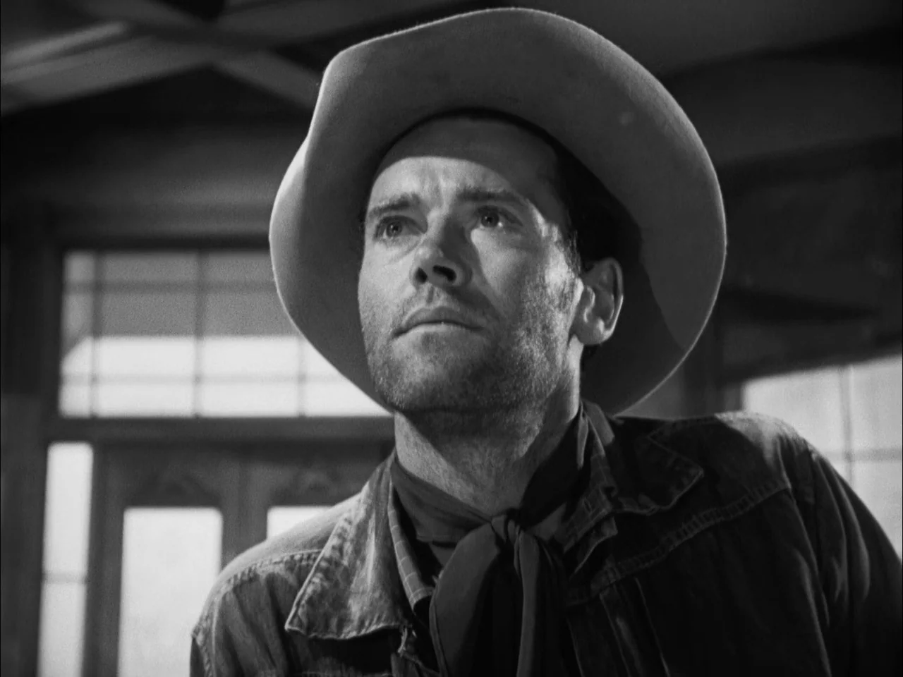 The Ox-Bow Incident (1942) movie still: closeup — A wooden interior space with a grid-paned window visible in the blurred background. A man wearing…