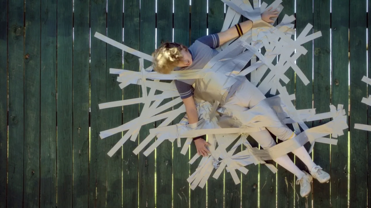 Everybody Wants Some!! (2016) movie still: fullbody — A vertical wooden fence made of dark green painted planks serves as a backdrop. A young male…