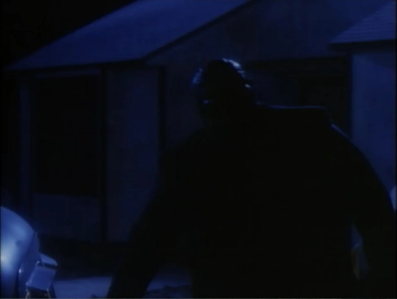 Cast a Deadly Spell (1991) movie still: medium — A residential exterior at night with a blue-tinted house structure in the background. A dark,…