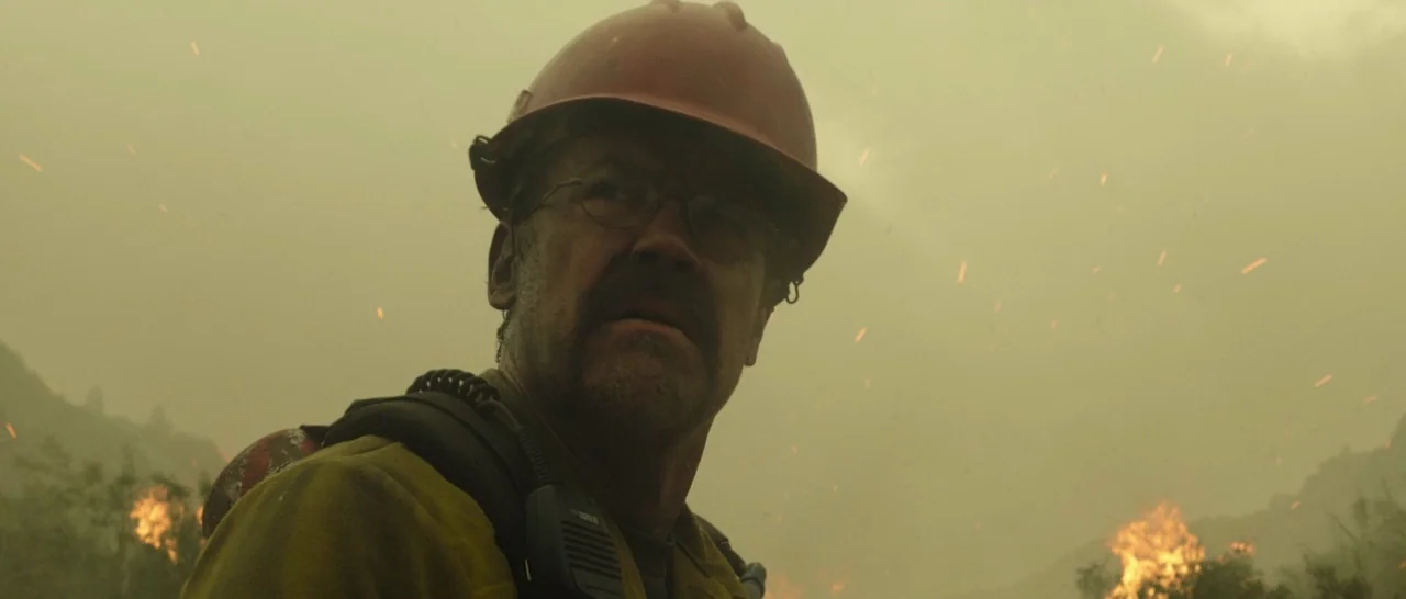 Only The Brave (2017) movie still: medium — A man in safety gear stands in a smoky outdoor area near burning terrain. Embers drift through the hazy…