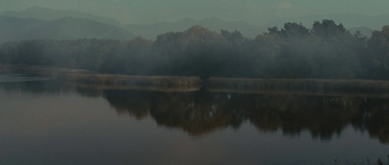 Snow White and The Huntsman (2012) movie still: establishing — A calm lake sits in the foreground with reeds lining the shoreline. Dense forest and…