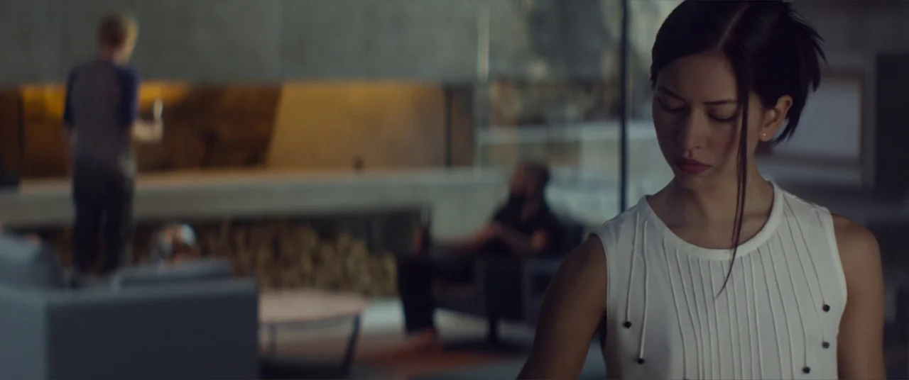 Ex Machina (2015) movie still: medium — A spacious, modern room features concrete walls and minimalist furniture in dim lighting. A woman stands in…