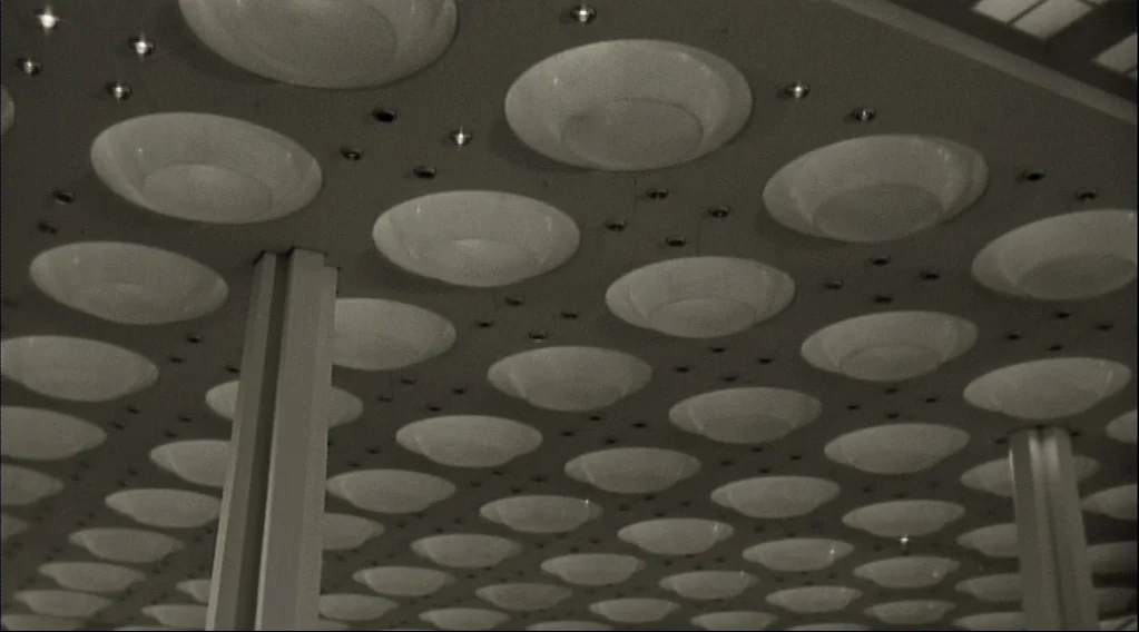 Wings Of Desire (1987) movie still: establishing — A low-angle view of a vast ceiling covered with repetitive circular light fixtures. Two vertical…