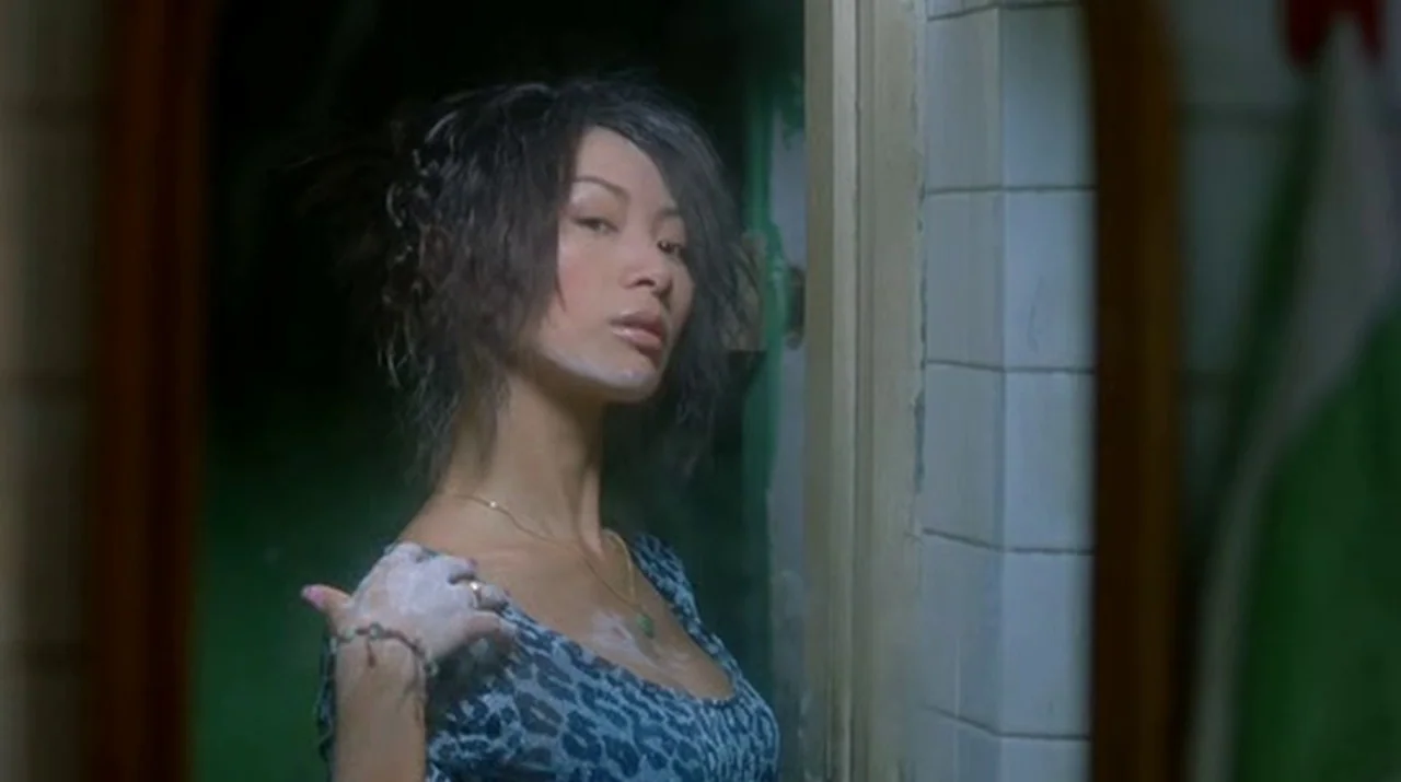 Dumplings (2004) movie still: medium — A woman stands in a tiled bathroom looking at her reflection in a mirror. She has white cosmetic cream on her…