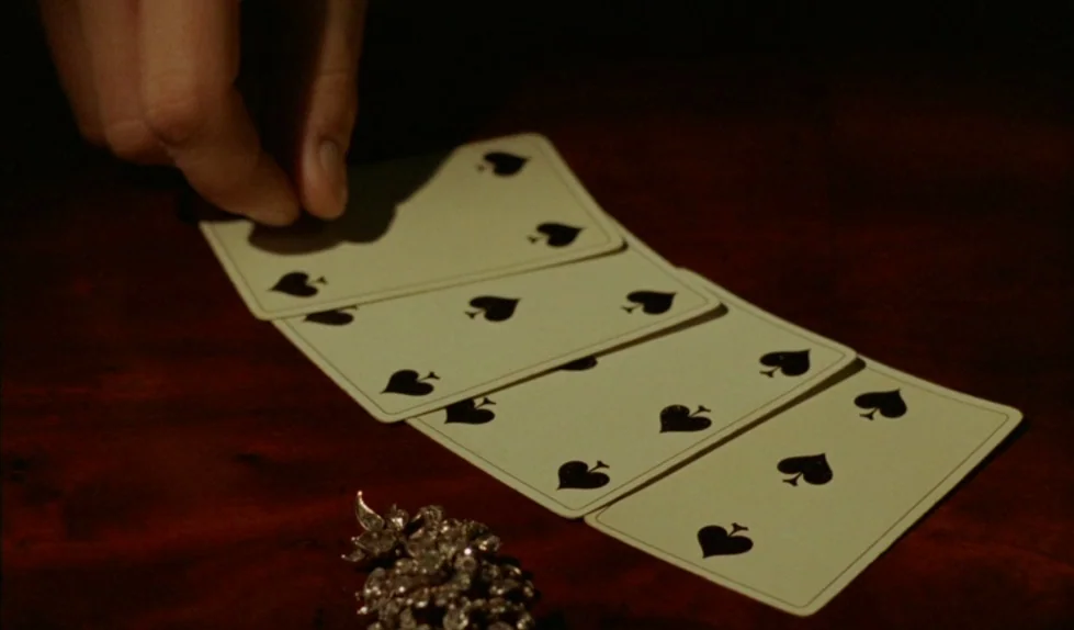 Elvira Madigan (1967) movie still: closeup — A dark wooden surface holds several playing cards arranged in a row. A silver broach decorated with…