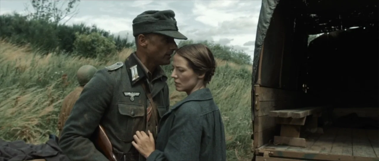 Sin retorno (2009) movie still: medium — An open field with tall grass and a parked military truck in the background. A soldier in a 1940s uniform…