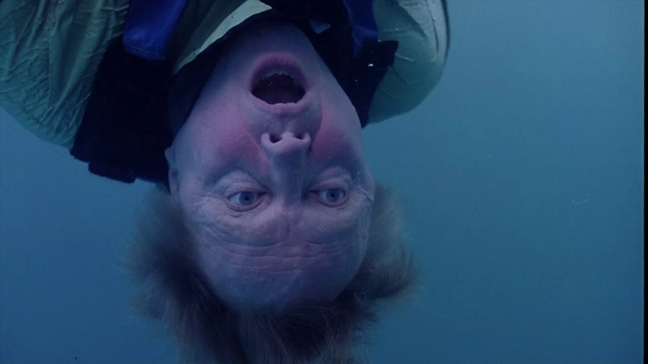 The Manchurian Candidate (2004) movie still: closeup — A man is submerged upside down in deep blue water. He floats motionless with his mouth open…
