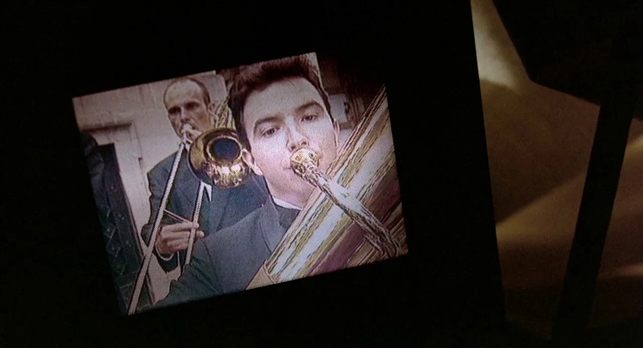 Three Colours: Blue (1993) movie still: medium — A small, low-resolution screen displays a recording of two men playing brass instruments. The…