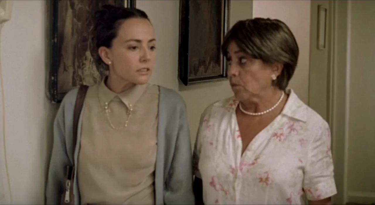 Sex, Love And Other Perversions II (2006) movie still: medium — A residential hallway with framed artwork on a white wall. Two women stand…