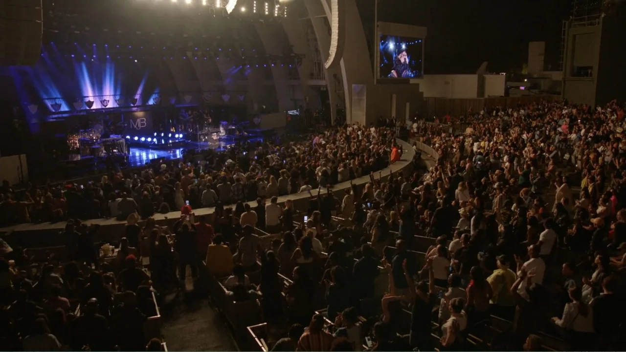 Mary J. Blige's My Life (2021) movie still: wide — A large outdoor amphitheater at night with a packed crowd facing a stage. Bright stage lights…