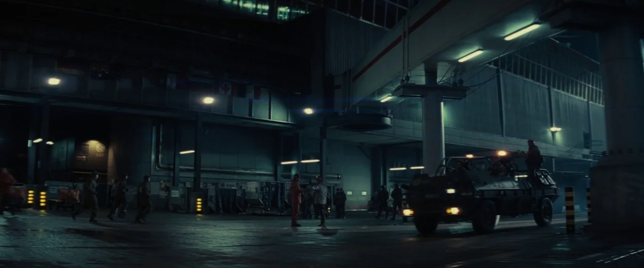 Edge of Tomorrow (2014) movie still: wide — A nighttime military compound features concrete architecture, overhead walkways, and rows of…
