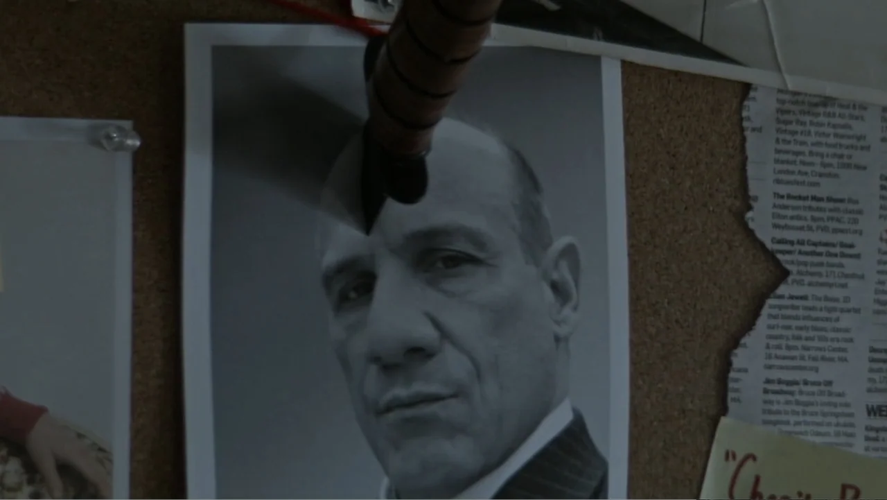 The Collective (2023) movie still: closeup — A brown cork bulletin board displays a black and white photograph and news clippings. A metal knife…
