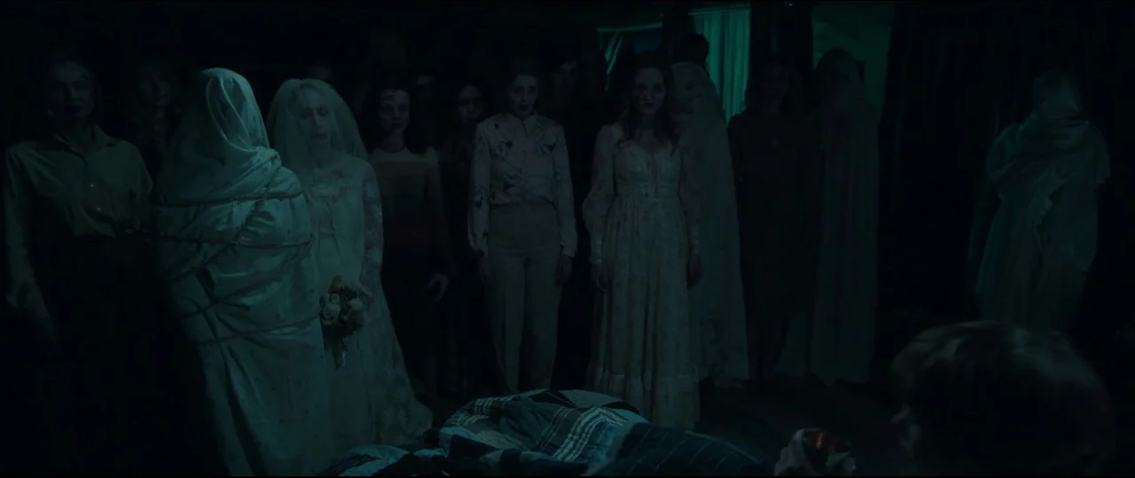 Insidious: Chapter 2 (2013) movie still: wide — A dark bedroom holds a group of pale women standing together in a circle. They remain stationary,…