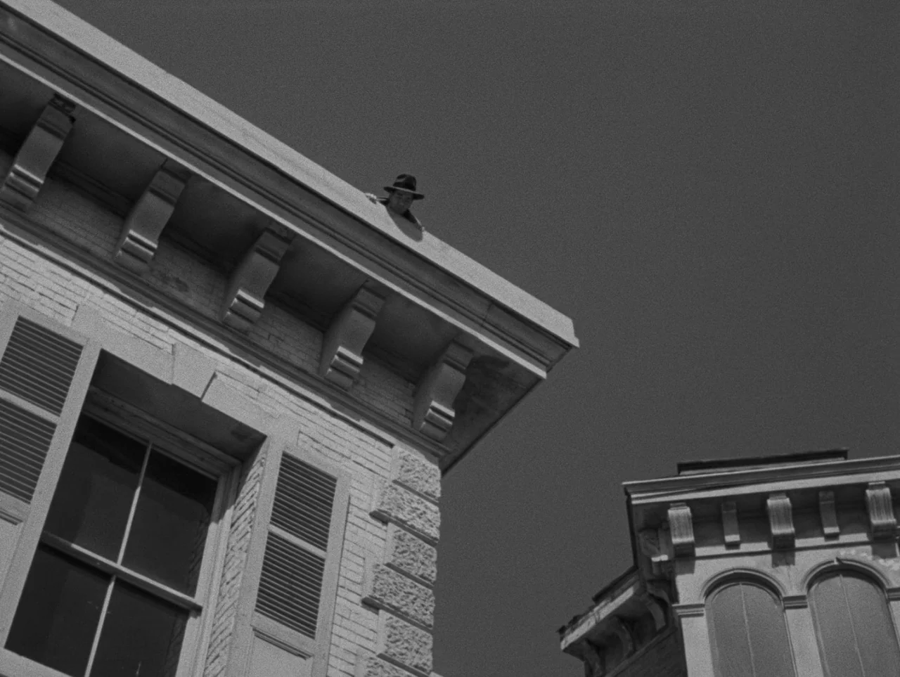 Pickup on South Street (1953) movie still: wide — A low-angle view of stone building cornices against a clear, dark sky. A man wearing a fedora hat…