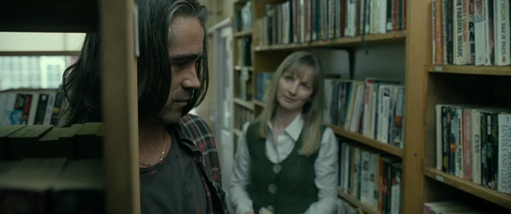 Ondine (2009) movie still: medium — A cluttered library aisle features wooden shelves packed with various books and novels. A man stands in the…