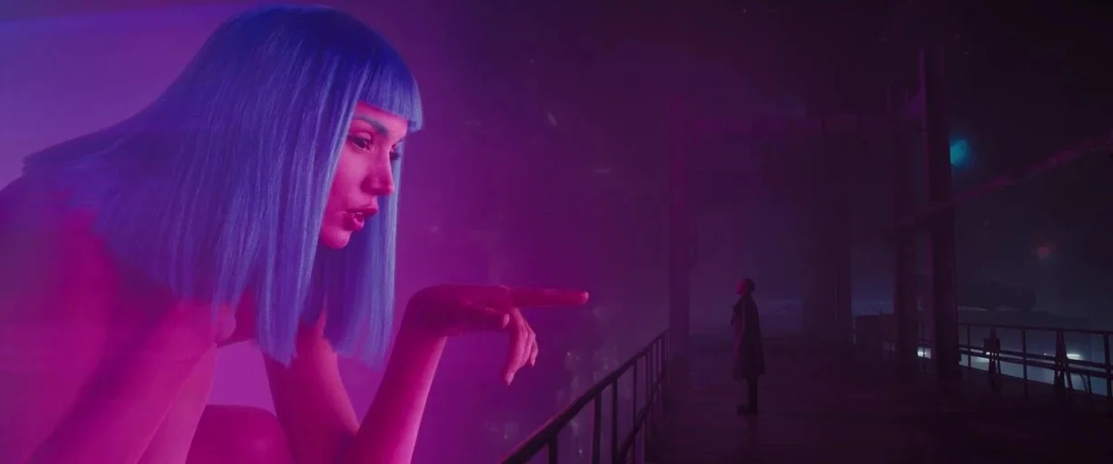 Blade Runner 2049 (2017) movie still: wide — A wet, dark outdoor balcony overlooks a blurred neon city in deep fog. A massive, translucent…