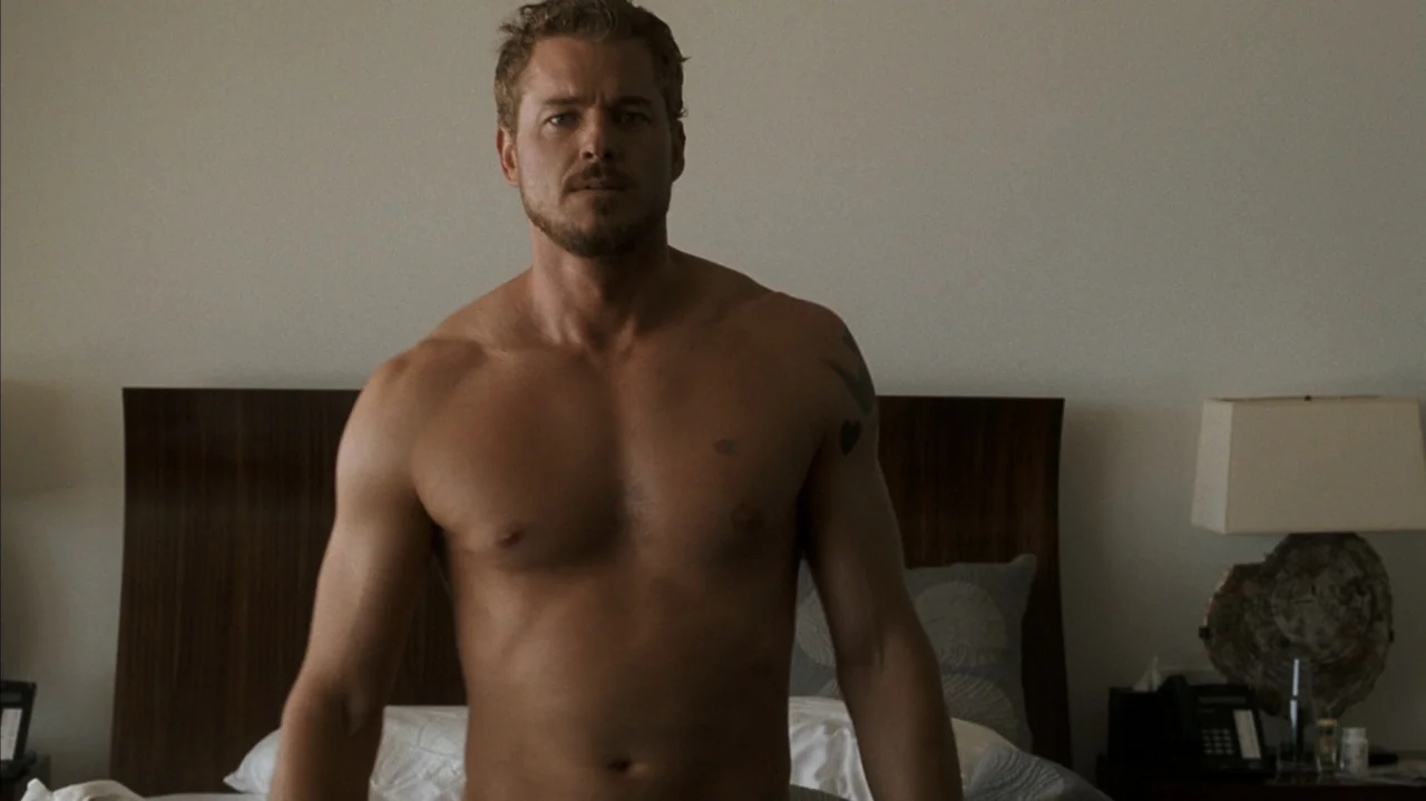 F Valentine's Day (2026) movie still: medium — A modern hotel room with a wooden headboard and a bedside lamp visible. A shirtless man stands in…