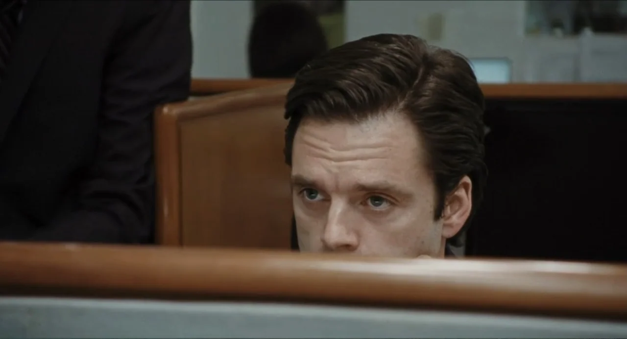 A Different Man (2024) movie still: closeup — An office environment features partitions and desks in a professional workplace setting. A man in a…