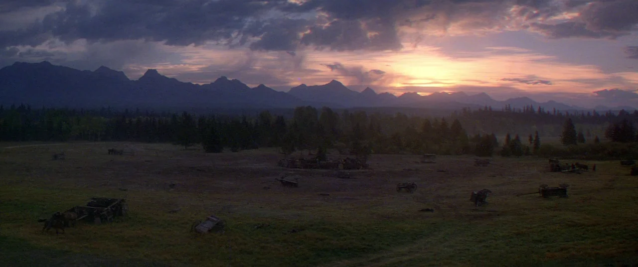 Heaven’s Gate (1980) movie still: establishing — A vast, open plain lies before a distant, jagged mountain range at twilight. Scattered remnants of…