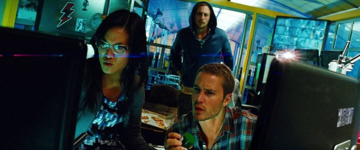 Savages (2012) movie still: medium — A cluttered room filled with computers and surveillance monitors displaying multiple feeds. Three individuals…