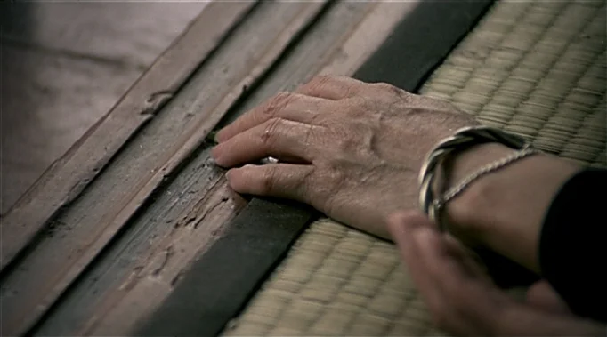 A Time To Love and A Time To Die (1985) movie still: closeup — A close-up of a human hand resting on the wooden threshold of a doorway. The textured…