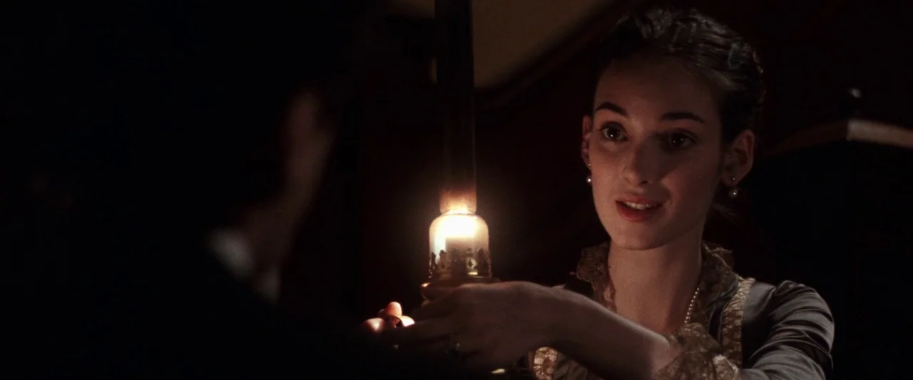 The Age of Innocence (1993) movie still: medium — A dim room is illuminated by the glow of a handheld oil lamp. A young woman in period attire looks…