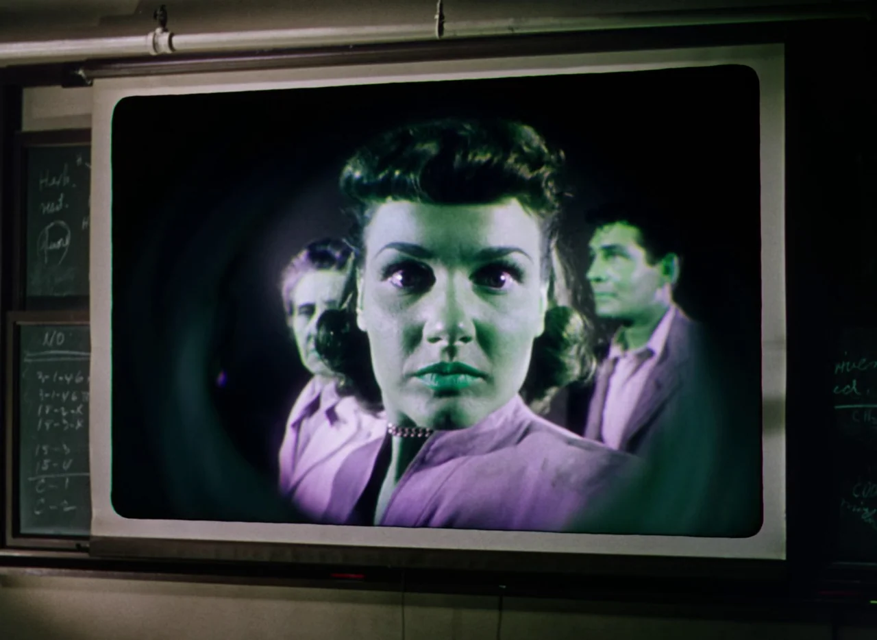 The War of the Worlds (1953) movie still: closeup — A projection screen displaying an image of three people sits in a darkened room. The woman in…