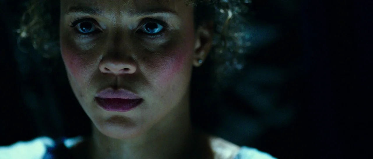 The Purge: Anarchy (2014) movie still: closeup — A woman's face is illuminated by a cold light source in a dark space. She stares directly into the…