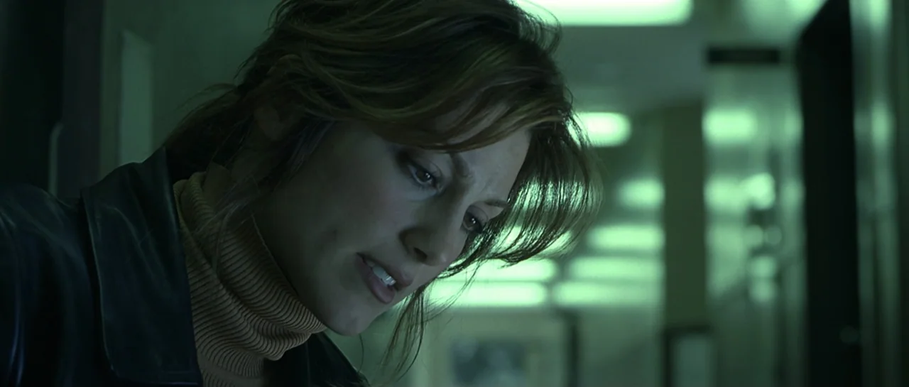 Don't Say a Word (2001) movie still: closeup — A modern office hallway with long fluorescent lights glowing in the blurred background. A woman in a…