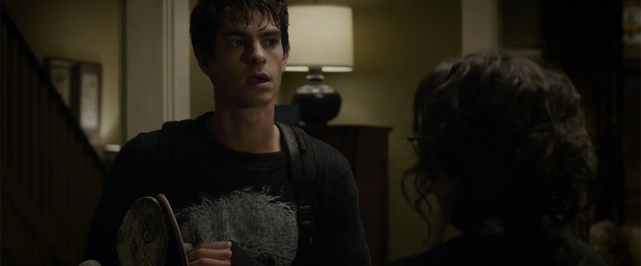 The Amazing Spider-Man (2012) movie still: medium — A dimly lit residential interior features a table lamp glowing in the background. A young man…