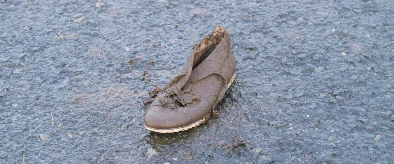 A White, White Day (2019) movie still: closeup — A single mud-covered shoe lies on the surface of a wet asphalt road. The shoe is oriented toward…