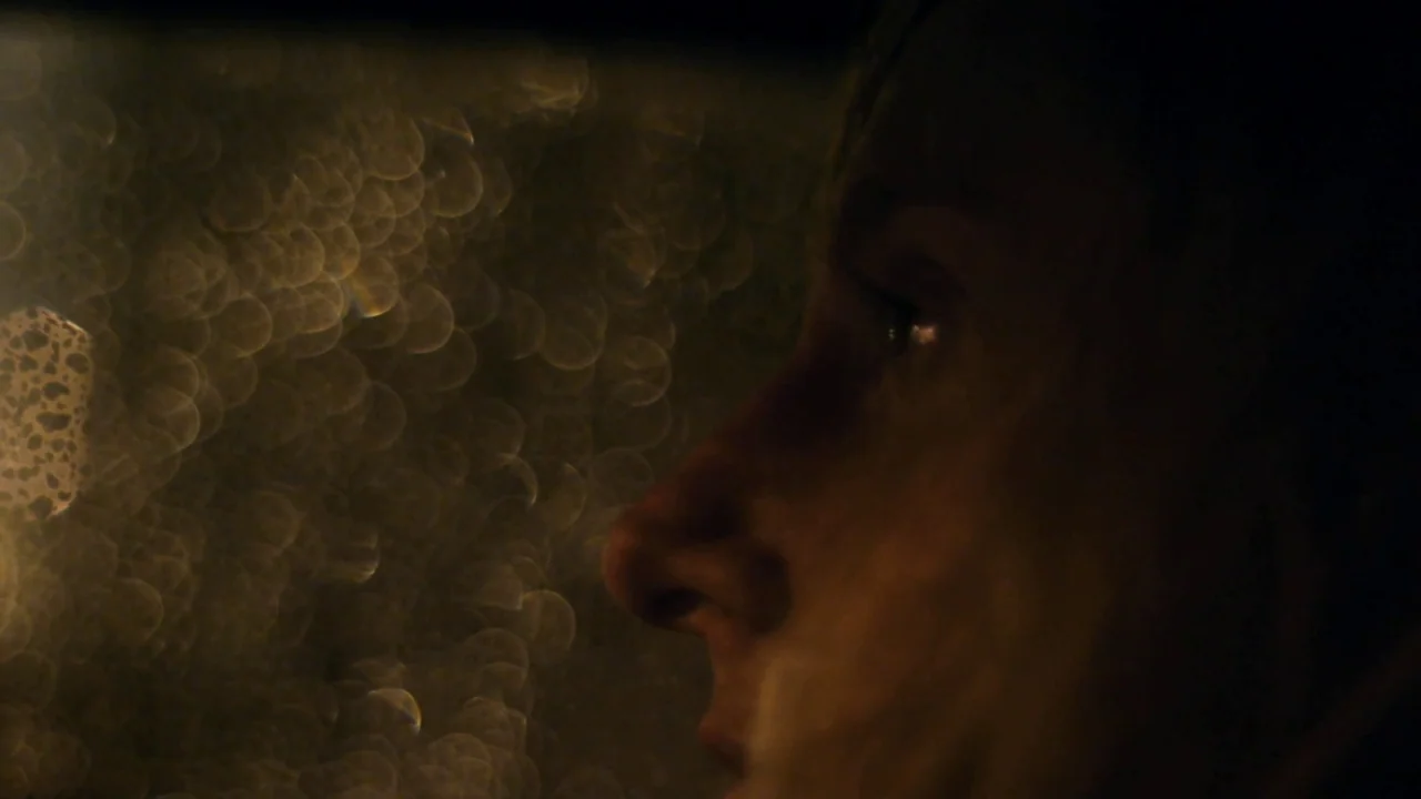 Counting (2015) movie still: closeup — The interior of a vehicle at night with water droplets on the glass window. A young man sits in the passenger…