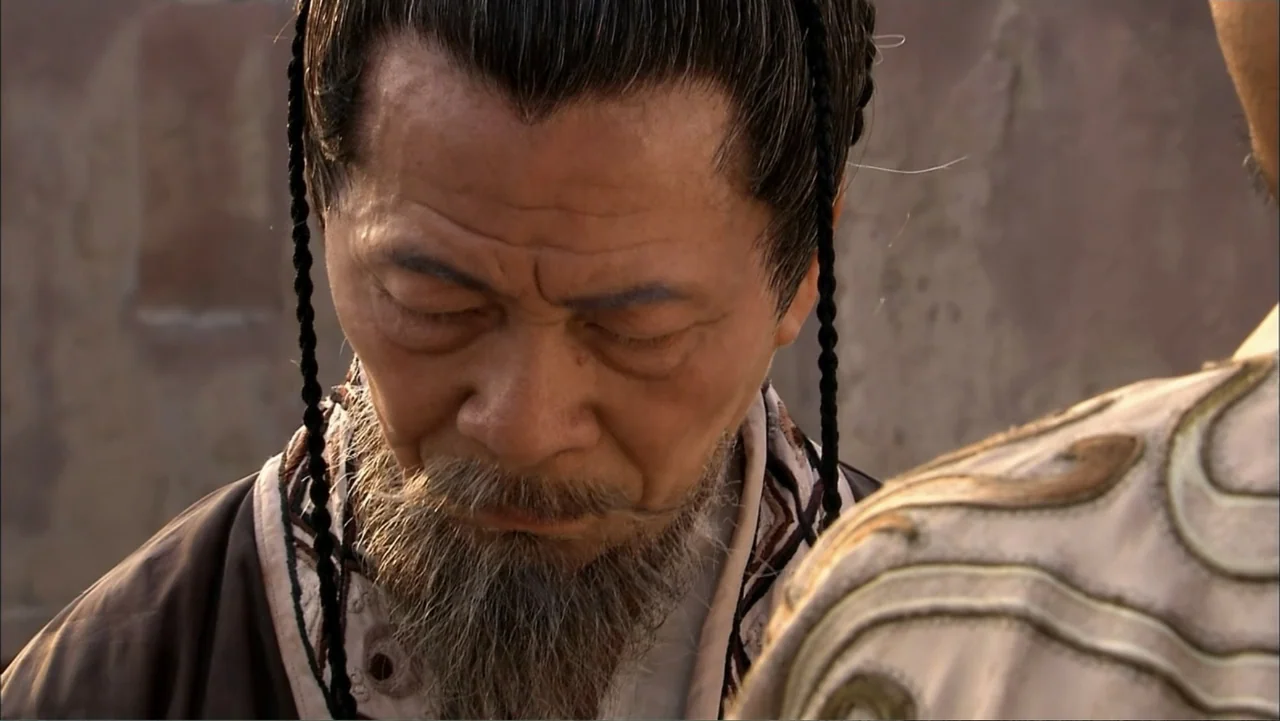The First Emperor (2006) movie still: closeup — An outdoor area with a textured stone wall background during late afternoon light. An elderly man in…