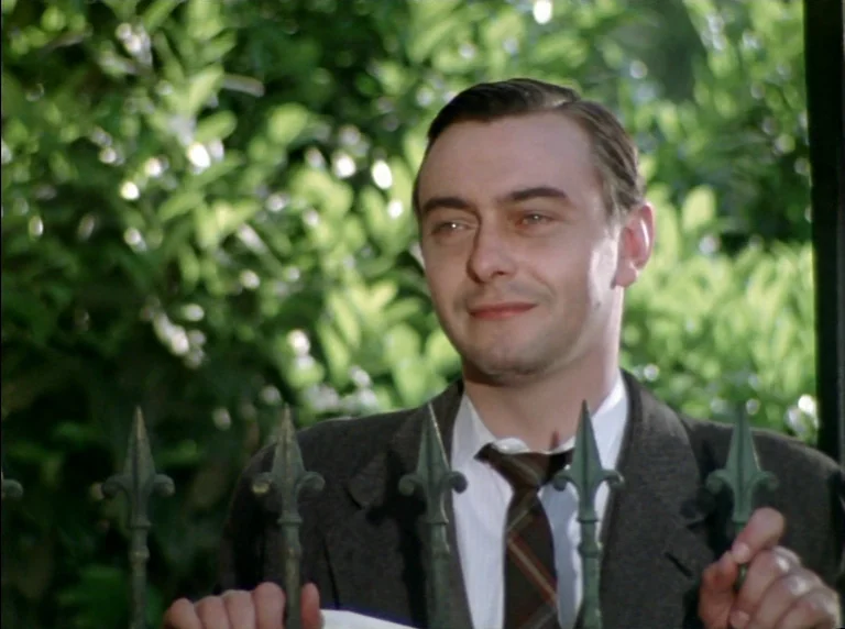 Fear Of Fear (1975) movie still: medium — A man stands behind a pointed metal fence in front of dense green bushes. The man looks off-camera while…
