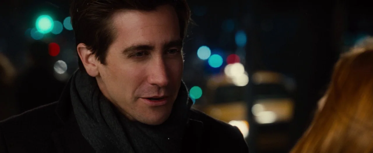 Nocturnal Animals (2016) movie still: closeup — An outdoor city street at night with blurry traffic lights in the background. A man in a dark coat…