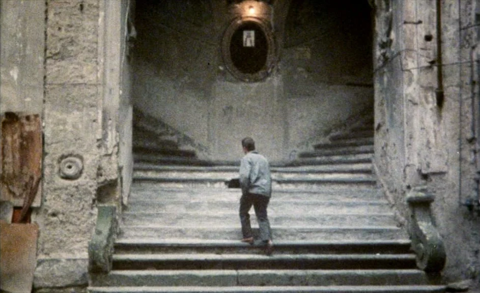 The Kingdom of Naples (1978) movie still: fullbody — A weathered stone staircase splits into two paths beneath a dimly lit arched wall. A man in a…