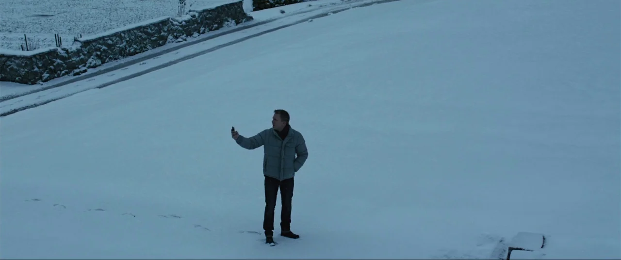 The Girl With The Dragon Tattoo (2011) movie still: wide — A vast, snow-covered open landscape borders a stone wall under an overcast sky. A man…